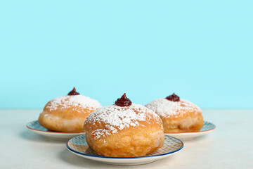 Plates with tasty donuts for Hanukkah celebration on light table against color background