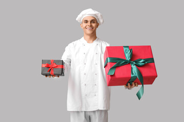 Male chef with Christmas gift boxes on grey background