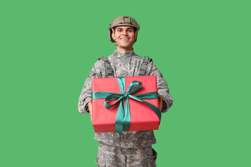 Male soldier with gift box on green background