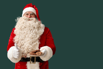 Santa Claus with plate of tasty cookies showing thumb-up on green background