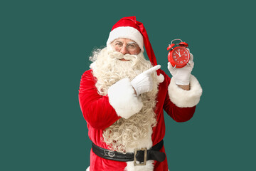 Fototapeta na wymiar Santa Claus pointing at alarm clock on green background