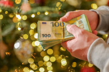 euro money in hands on a Christmas trees background.Christmas and New Year expenses. Spending on...