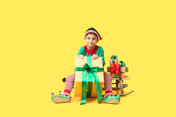 Cute little elf with sled and Christmas gifts on yellow background