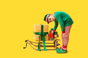 Cute little elf with sled and Christmas gifts on yellow background