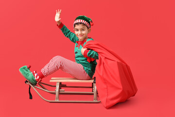 Cute little elf with sled and bag of gifts waving hand on red background
