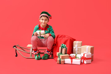 Cute little elf with sled and Christmas gifts on red background