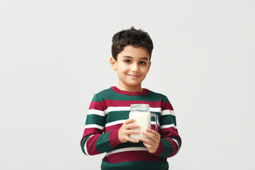 Cute little boy with mason jar of milk on white background