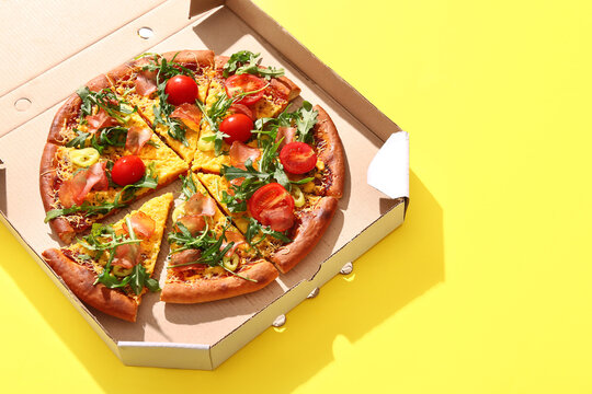 Cardboard box of delicious pizza with tomatoes and arugula on yellow background