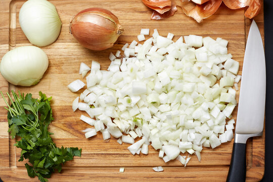 Chopped raw onions and herbs on a wooden cutting board with a chef's knife. Fresh gourmet ingredients.