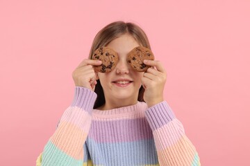 Girl covering eyes with chocolate chip cookies on pink background
