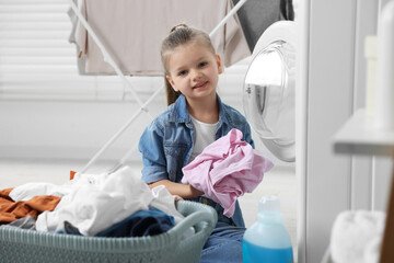 Little girl putting dirty clothes into washing machine in bathroom