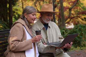 Fototapeta premium Affectionate senior couple with laptop spending time together in autumn park