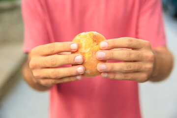 A man's hand holds a round bun, snack and fast food concept. Selective focus on hands with blurred background