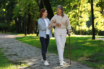 Senior lady with walking cane and young woman in park