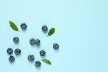 Tasty fresh blueberries with green leaves on light blue background, flat lay. Space for text