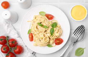Delicious pasta with brie cheese, tomatoes and basil leaves on white tiled table, flat lay