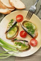Delicious sandwiches with sprats, pickled cucumber and green onion served with tomatoes on wooden table, flat lay