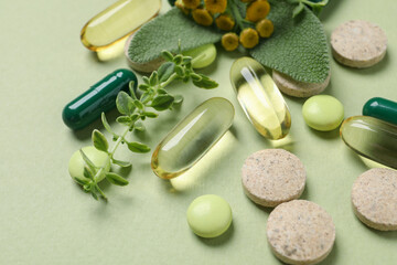 Different pills and herbs on light green background, closeup. Dietary supplements