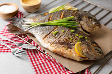 Seafood. Delicious baked fish served with green onion and lemon on light table, closeup