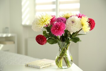 Bouquet of beautiful Dahlia flowers in vase and notebook on white table indoors. Space for text