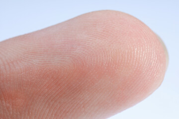 Finger with friction ridges on light blue background, macro view