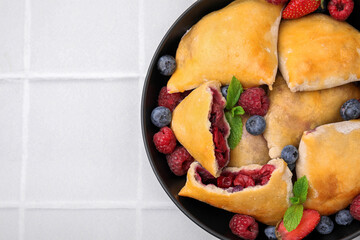 Bowl with delicious samosas, berries and mint leaves on white tiled table, top view. Space for text