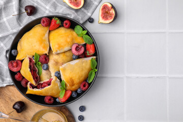 Bowl with delicious samosas, berries, fig and mint leaves on white tiled table, flat lay. Space for...