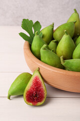 Cut and whole fresh green figs on white wooden table near grey wall