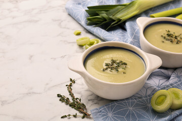 Tasty leek soup in bowls on white marble table, space for text