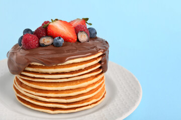 Stack of tasty pancakes with fresh berries and chocolate spread on light blue background, closeup. Space for text