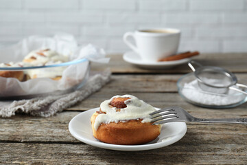 Tasty cinnamon roll with cream on wooden table. Space for text