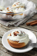 Tasty cinnamon roll with cream on wooden table. Space for text