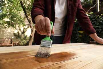 Man applying wood stain onto wooden surface outdoors, closeup