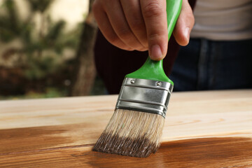 Man applying wood stain onto wooden surface against blurred background, closeup