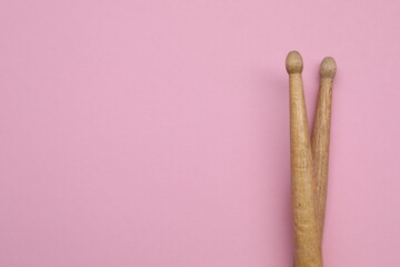 Two wooden drum sticks on pink background, top view. Space for text