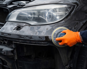 A mechanic sands the putty on a car body with a machine. Repair after an accident. 