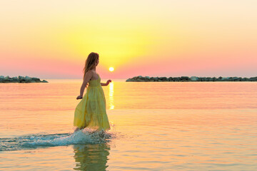 Fototapeta na wymiar Beautiful woman walking in water wearing a yellow colorful dress.