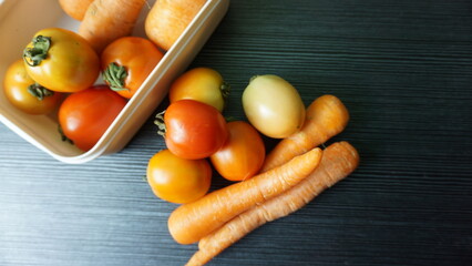 Fresh tomatoes and carrots on the wooden desk, with dark texture background.