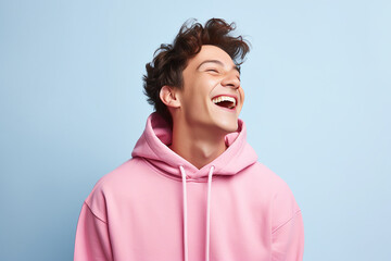 The portrait of a cute and handsome male teeager in a pink, blue hoodie standing and looking at the camera, isolated on a pink, blue background. Generative AI.