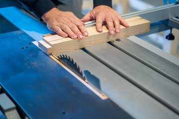 Closeup shot, man cutting peace of wood on a industrial table saw  - obrazy, fototapety, plakaty