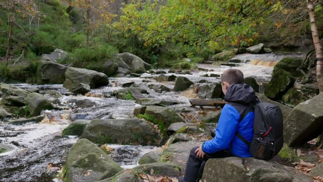 Young boy, camera and tripod, captures serene autumn-winter woodland, meandering stream. Outdoor photography adventure.