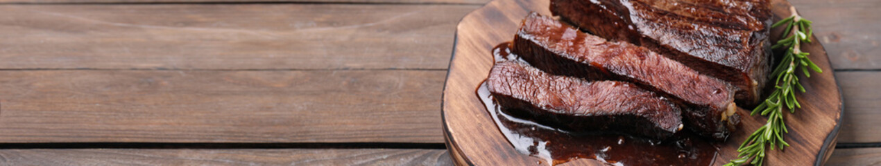 Delicious fried beef meat with rosemary on wooden table, space for text. Banner design