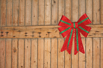 Rustic Christmas image of a red and green shiny bow hanging on a wooden wall intentionally offset...