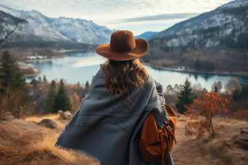 Happy woman in the mountains. Traveling woman standing in the wild with map against amazing view. Wearing hat, poncho and backpack. Snowfall in mountains. Wanderlust