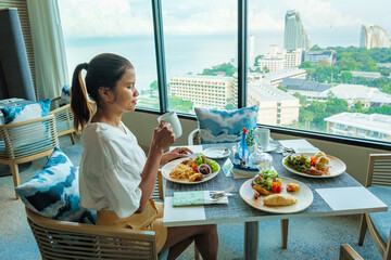 Asian Thai woman eating breakfast in a luxury hotel in Thailand, women drinking coffee looking out...