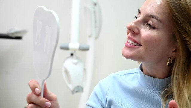 Young Handsome woman after Dental Whitening process smile in mirror. Teeth whitening with UF Lamp, Led Lamp and gel in Dental Clinic. 4k 120 fps slow motion Raw footage