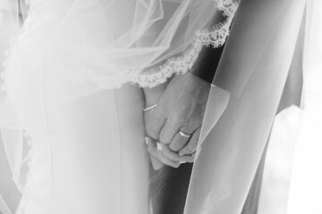 A black and white portrait of a bride and groom holding hands underneath a lace veil on their...
