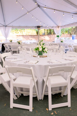 A white table and chairs set up at a wedding reception with a simple floral arrangement in the middle