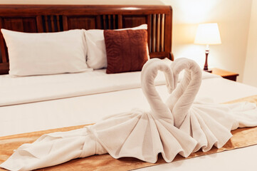 White rattles were rolled together in the shape of a swan and placed on a mattress on a wooden bed with lamps on either side of the bed.