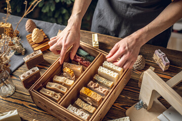 A woman soap maker holds handmade soap in her hands. A lot of different sliced pieces in a wooden...